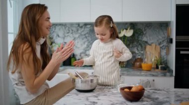 Cheerful family making dough at home. Smiling mother talking with child at kitchen. Adorable preschooler girl doing bakery helping millennial mom. Homemade food and little helper concept