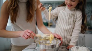 Mother daughter hands creating dough at home close up. Positive family preparing pastry together at kitchen. Smiling woman mixing whisk spending time with child. Mommy teaching lovely kid to cook
