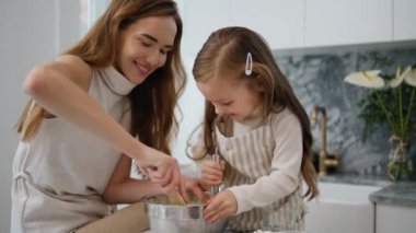 Adorable child helping mom at kitchen closeup. Positive family having fun cooking dessert together. Mother daughter whisking dough making holiday cookies. Happy woman teaching cute kid baking pastry