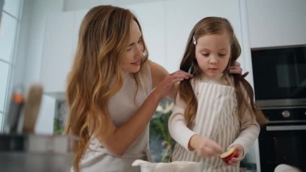 可爱的孩子与妈妈在家特写镜头做苹果派 慈爱的母亲温柔地把女儿的头发直放在厨房里 周末全家一起做饼干 小孩帮妈妈做家务 — 图库视频影像