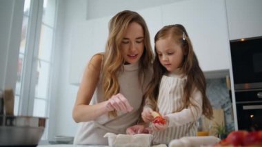 Meraklı kız, annesiyle birlikte mutfakta pasta dekore ediyor. Sevgi dolu bir kadın, çocuklara evde yemek yapmayı öğretir. Arkadaş canlısı bir aile tatlı pişiriyor. Bekar anne ve kız bebek birlikte eğleniyorlar.