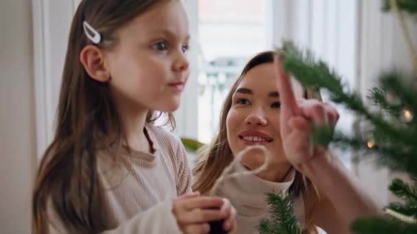 可爱的孩子把圣诞礼物放在树枝上的肖像上 可爱的女人用手指帮助孩子装饰家里的圣诞树 积极准备新年派对特写的亲生女儿 — 图库视频影像