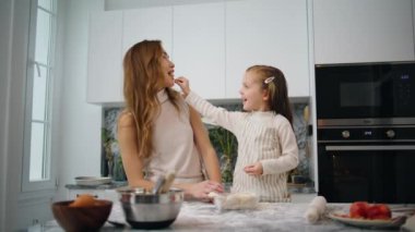 Annesini elmayla besleyen tatlı bir kız. Modern iç mekanlarda küçük çocuklara meyve veren gülen bir kadın. Pozitif aile, rahat bir dairede birlikte yemek yaparken eğleniyor.