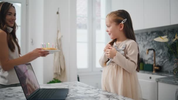 年轻的母亲在厨房特写处祝贺女儿 可爱的孩子拿着蜡烛看着生日蛋糕 家庭视频在笔记本电脑前打电话给父亲 准备许愿的小女孩 — 图库视频影像