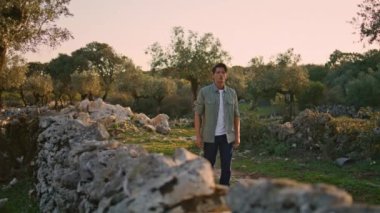 Rahat adam taş çit bahçesinden geçerken yakın plan. Ciddi bir adam zeytin ağaçlarının fidanlarını arıyor yaz yolunda tek başına dolaşıyor. Çiftlik işçisi, sakin ve kadim duvarlarda, sıcak ışıkta yürüyor. Kırsal yaşam tarzı