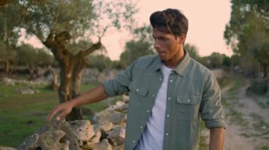 Bahçe portresindeki taş duvara dokunan düşünceli adam. Rahatlamış adam yaz doğasında yürüyüş mesafesine bakıyor. Bronzlaşmış köy işçisi ağaçlarda dinlenirken temiz havanın tadını çıkarıyor.