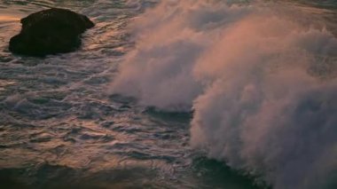 Splashing waves covering rock at sunset closeup. Cold sea water foaming at evening shore. Swirling aqua washing stone at high ocean. Stormy liquid disturbing surface. Marine nature detail concept