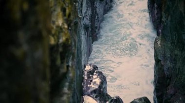 Waves breaking at ocean cliff surface closeup. Water splashing at empty stone place. Cold sea foaming between dark rocks landscape. Bubbling aqua swirling at morning. Picturesque marine nature concept
