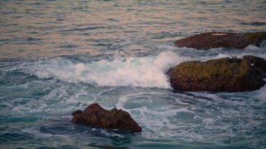 Foamy waves rolling on dark rocks closeup. Beautiful seascape with high stones ocean surface. Swirling aqua amazing landscape at morning nature. Water breaking at summer seacoast. Calmness concept
