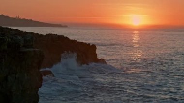 Warm sunrise cliffside nature. Mountain hill silhouette at morning sea beach. Golden sunshine illuminate dark hill with calm ocean water. Rocky coastline with orange skyline. Marine landscape concept 