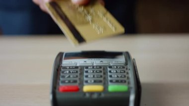 Man hands making contactless payment with credit card at machine terminal on table close up. Unknown client paying bill by touching card to wireless reader bank pos device. Cashless nfc technology.