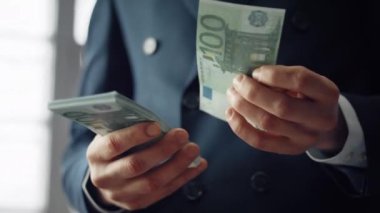 Unknown man counting hundreds euro indoors close up. Successful rich businessman calculating european bills wearing black suit. Male hands holding pack of money cash. Business finance economy concept.