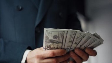 Dolarları tutan adam elleri kapalı. Zarif siyah takım elbiseli tanınmayan bir işadamı 100 dolarlık banknotları olan bir çanta taşıyor. Başarılı yatırım kârı çalışan maaşı kavramı.