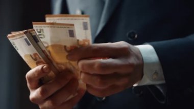 Closeup man hands counting money denomination of fifty euro indoors. Unknown businessman in elegant black suit calculating cash american currency from business investment. Financial success concept.