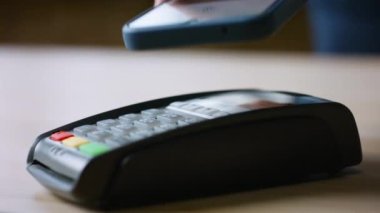 Nakitsiz alım için NFC teknolojisini cep telefonunda kullanan bir adam. Bilinmeyen kişi, akıllı telefonuyla terminaldeki kart okuyucuya dokunarak ücretsiz ödeme yapıyor. Elektronik para ödeme kartı konsepti