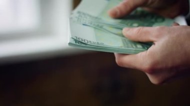 Unrecognizable man counting hundred euro bills in office close up. Male hands holding wad of european currency banknotes. Young businessman calculating money cash indoors. Business income concept.