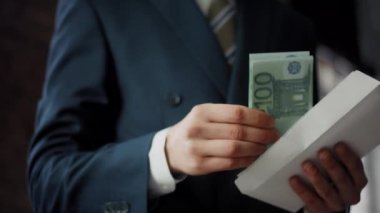 Unrecognizable man putting bribe money into envelope in office close up. Businessman hands placing cash hundreds euro into envelope for corruption deal. Illegal income bribery financial crime concept.