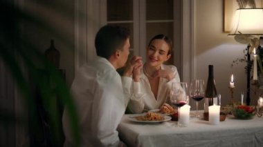 Young spouses flirting at night candles room closeup. Smiling woman enjoying man touches at cozy interior. Relaxed pair drinking wine celebrating anniversary. Cheerful lovers having romantic evening