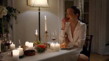 Relaxed woman eating at evening date restaurant close up. Calm lady enjoying romantic dinner at candles table. Smiling girl tasting anniversary meal at night atmosphere. Model at warm light apartment