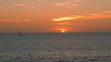 Calm ocean sunset view in summer. Lonely yacht boat sailing in peaceful water on golden sunrise hour. Beautiful relaxing sea horizon landscape in morning. Tranquil paradise evening at seashore concept