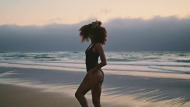 African american girl performer dancing on gloomy seashore at summer evening. Flexible young woman moving body smoothly enjoying windy twilight. Curly brunette performing contemporary style on nature.