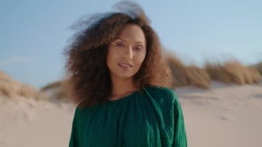 Kum çölünde yaz günü gülümseyen Afrikalı Amerikalı güzel bir kızın portresi. Modern makyajlı genç ve çekici bir kadın kameraya bakıyor. Kumullara bakıyor ve çimenleri kuruyor. Doğada zaman geçirmek..