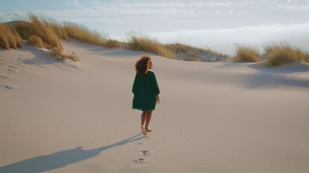 黒いドレスで砂漠の砂丘を歩くアフリカ系アメリカ人の女性をバックビューします 砂の上を歩く無名の少女夏の風の強い日の足跡を作る リラックスした巻きブルネットは荒野で美しい自然を楽しむ — ストック動画