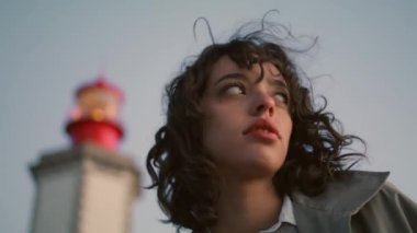Portrait worried girl posing at night lighthouse view. Thoughtful curly woman resting seaside contemplate personal crisis in evening. Unhappy lonely teenager feel insecure. Melancholy solitude concept