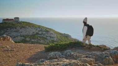 Hiking girl talking phone at calm ocean sunset. Excited tourist walking mountain with backpack using smartphone. Adventure woman enjoy active vacation trekking sea cliff. Roaming communication concept