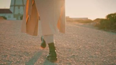 Girl legs walking road in sunlight closeup. Relaxed woman enjoy autumn evening at countryside. Unrecognized traveler stylish millennial strolling pathway resting on weekend. Chill out relaxation time