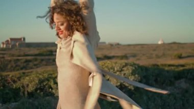 Beautiful girl spinning sunlight walking ocean cliff. Carefree woman enjoy life admiring sea peaceful landscape. Stress free joyful female stretching touching curly hair. Happiness freedom concept 