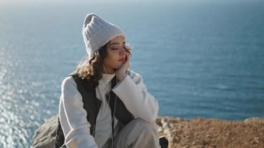Huzurlu kız okyanus uçurumunda müzik dinliyor. Hayalperest kadın, kapalı gözlerle rahatla hafta sonu gezisinde en sevdiği şarkıyı dinle. Güzel gülümseyen dişi deniz doğasına hayran. Stres konsepti yok.