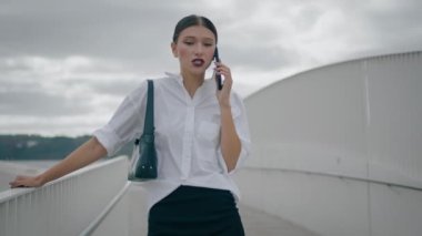 Stylish busy businesswoman giving phone instructions standing street in front cloudy sky. Worried dissatisfied woman solving work problems by telephone call. Lady boss hearing bad news by mobile talk.