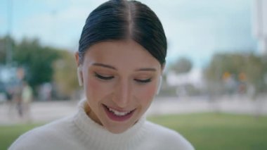 Smiling girl blogger recording vlog talking to camera closeup. Happy young woman in wireless earbuds talking making video call chatting distantly in internet app outdoors. Webcam view of speaking lady