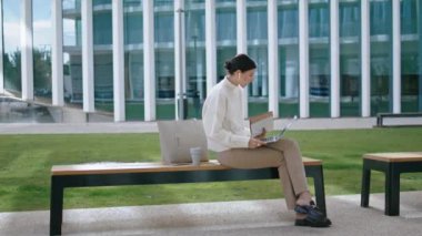 Confident successful businesswoman talking on video chat at laptop sitting bench outdoors. Smart elegant woman conducting online webinar using modern notebook on street near office. Lady work remotely