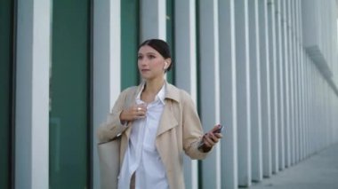 Pretty woman calling by wireless earbuds to friends walking city street. Emotional attractive girl laughing on phone conversation gesturing. Beautiful young lady talking by modern smartphone outdoors.