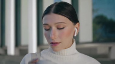 Attractive business girl tasting coffee takeaway on street work break close up. Portrait of beautiful young woman drinking beverage from paper cup. Business lady wearing wireless headset relaxing.