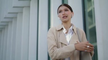 Confident smart woman communicating by wireless earbuds standing city street alone closeup. Young businesswoman consulting remotely using modern headset outdoors. Attractive girl talking by headphones