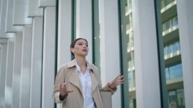 Confident woman calling by phone earbuds walking on city street close up. Busy businesswoman speaking mobile telephone going to office outdoors. Young lady using smartphone headset for communication.