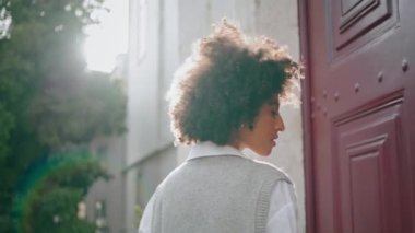 Sensual gorgeous woman posing at bright sunlight standing near red door city building closeup. Young attractive african american girl walk outdoors sunny day. Pretty model looking camera seductively.
