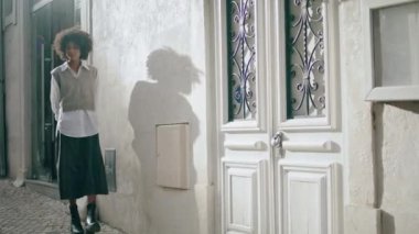 Gorgeous stylish girl exploring cozy city street on vacation. Brunette tourist walking beautiful old district sunny day. Attractive african american woman enjoy looking on town architecture outdoors.