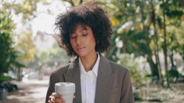 Confident african american woman drinking coffee in paper cup close up. Gorgeous businesswoman standing in beautiful city park alone . Attractive curly girl in business suit enjoying hot beverage. 