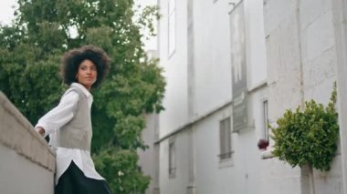 Serene cute girl dancing on empty city street. Attractive young african american woman spinning body having fun on town walk alone. Happy carefree brunette in white shirt enjoy weekend outdoors.