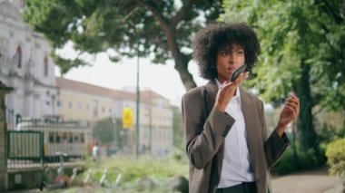 Şehir parkına yakın duran telefonda sesli mesaj dikte eden çok çekici bir kadın. Kendine güvenen Afro-Amerikan iş kadını açık havada akıllı telefon kullanıyor. Takım elbiseli şık bir kız dinamik konuşuyor..