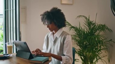 Confident african american girl working remotely in beautiful home office close up. Young curly woman chatting online using modern laptop. Attractive stylish lady using internet technology for job.