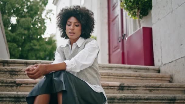 沉思宁静的女孩一个人坐在楼梯城街近旁 卷曲的非洲裔美国年轻女子穿着时髦的服装在户外放松 迷人时尚的黑发人散步后休息一下 — 图库视频影像