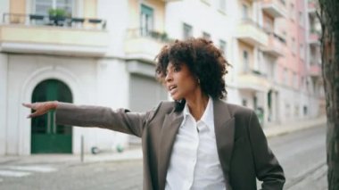 Şehir caddesinde duran taksiye binen çekici bir iş kadını. Kendine güvenen kıvırcık Afrikalı Amerikalı kız el sallıyor. Şehirde poz veren zarif ceketli güzel bir bayan.