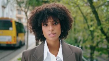 Şehir caddesinde şık bir takım elbiseyle poz veren kendine güvenen muhteşem bir manken. Çekici, şehvetli, Afro-Amerikan kadın yeşil ağaçların önünde. Genç ve güzel bir kız kasaba yolunda tek başına duruyor..
