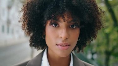 Awesome sensual girl face looking camera with light smile close up. Portrait of attractive african american woman with lush curly hairstyle posing at city street. Beautiful young lady relax outdoors.