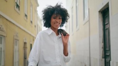Smiling businesswoman enjoy summer walk on cozy city street closeup. Attractive cheerful african american woman holding jacket on shoulder at relaxed stroll. Back view happy carefree girl raising hand